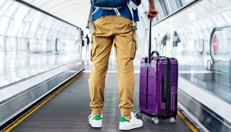 A man stands with a suitcase on a moving sidewalk in an airport