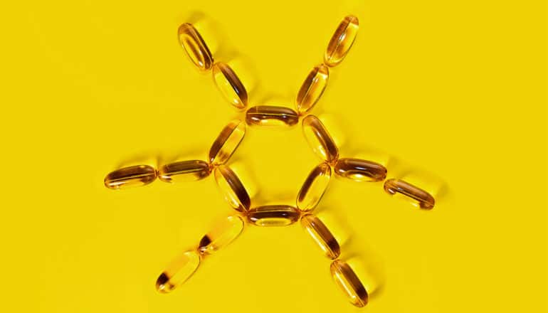 Vitamin D pills arranged in the shape of a sun on a yellow backrground