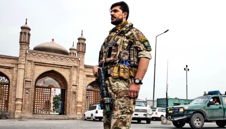 An Afghan security force member stands on the street in fatigues and carrying a gun