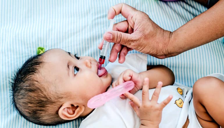 A parent gives their child antibiotics orally with a syringe