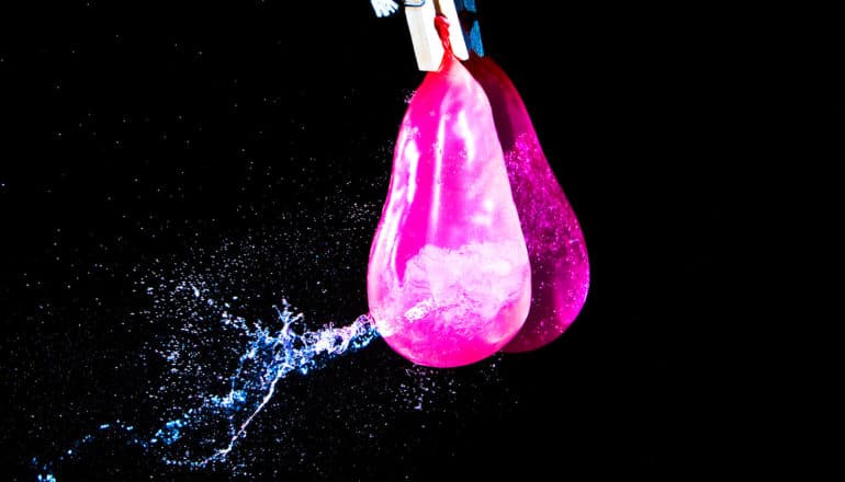 A pink water balloon leaks water on a black background