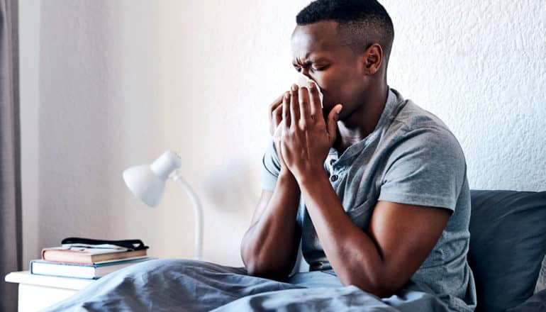 A man sits up in bed blowing his nose