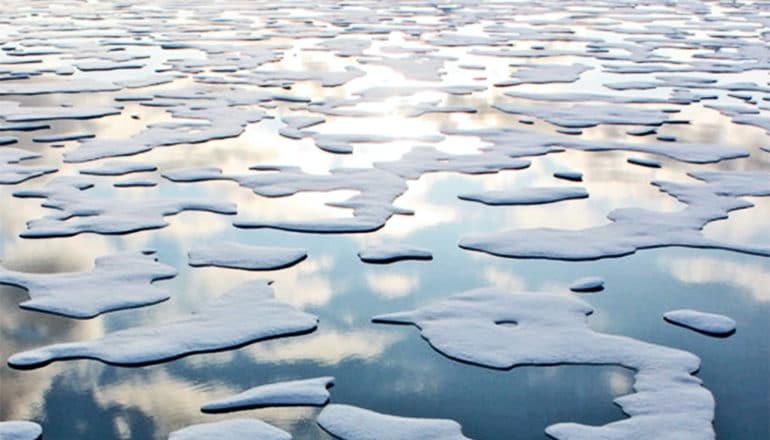 White sea ice in blue water with the sun setting reflected in the water