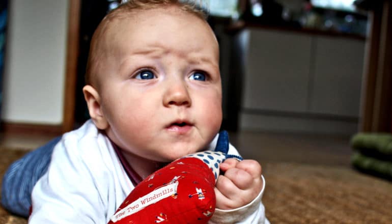 A baby on the floor looks up with a furrowed brow