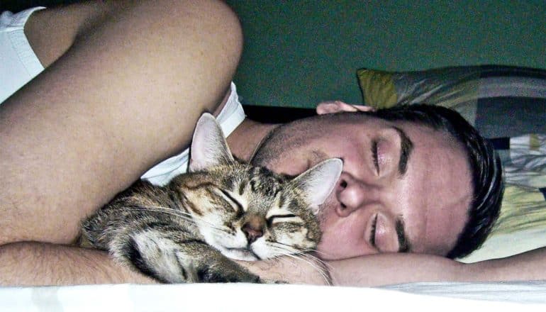 A man sleeps on his side while holding his sleeping cat