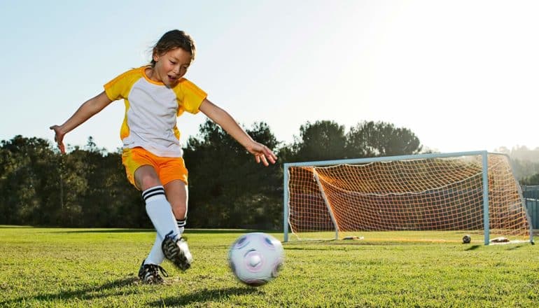 young girl looks proud and happy kicking soccer ball