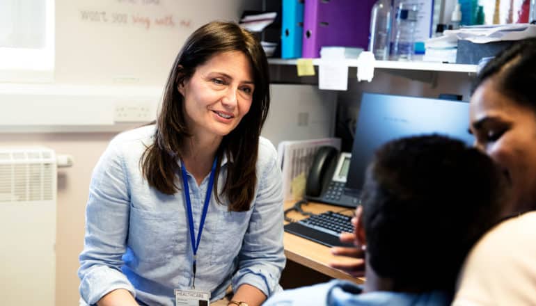 adult with lanyard speaks to adult holding child in cluttered office