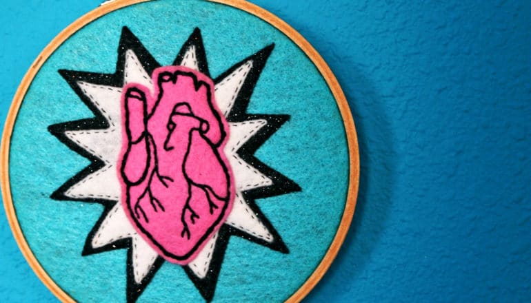 A pink heart stitched onto a blue fabric against a blue background