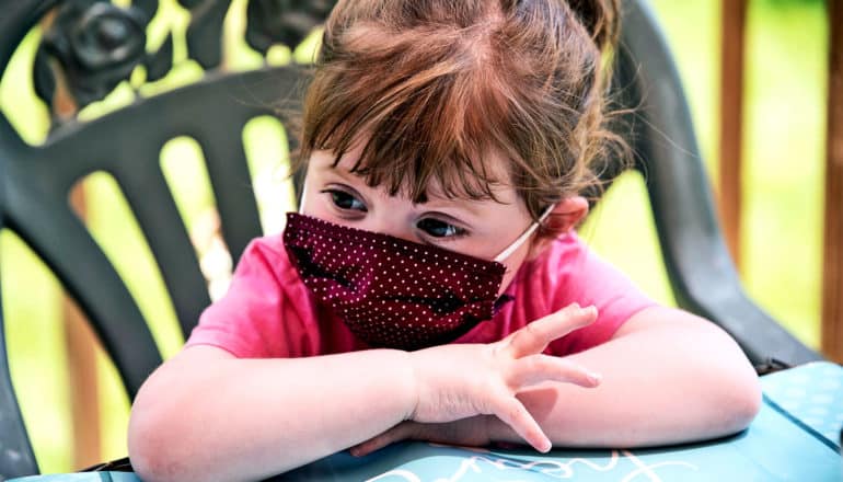 A young girl sitting in a chair with a mask on