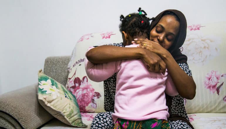 adult sitting on couch smiles while hugging child