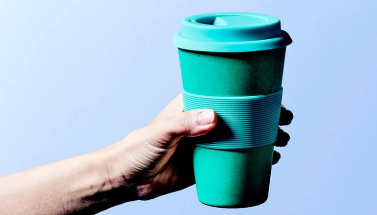 A person holds a green reusable coffee cup