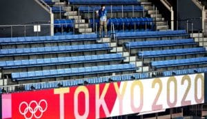 A single person in a sea of empty chairs in the stands at the Tokyo Olympics with a "Tokyo 2020" sign in red and white