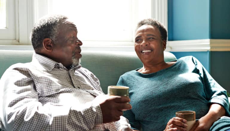 older Black adults smile on couch with coffee