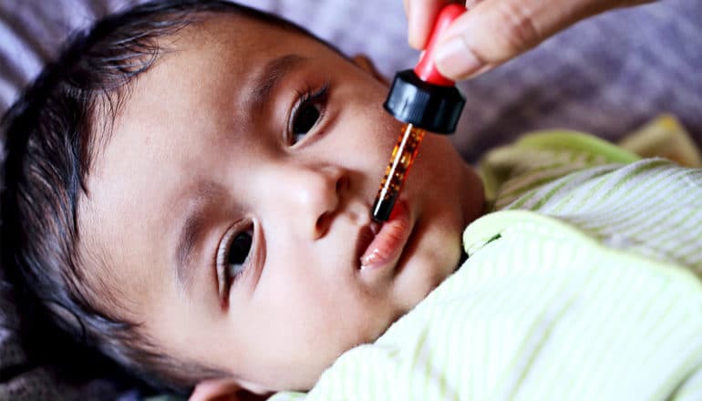 A parent gives a baby an oral vaccine by dropper