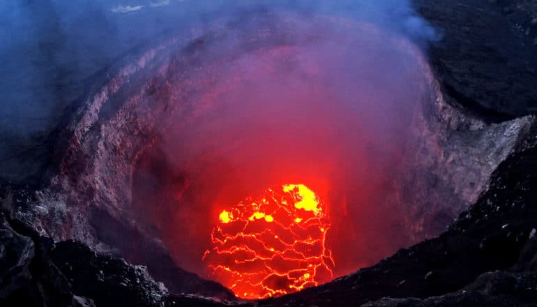 Smoke rises from the lave lake at the summit of Kilauea, with red lava visible in the crater