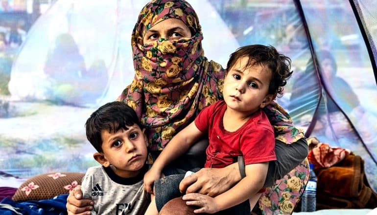 A mother holds her two children in a tent at a makeshift shelter