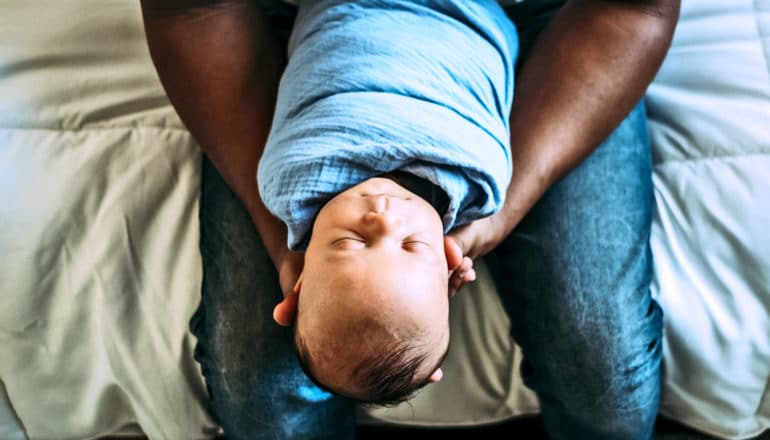 seated adult holds swaddled baby