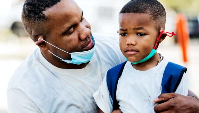 A father comforts his son outside with their face masks around their chins