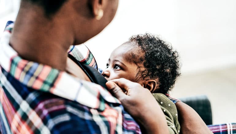 A mother in a plaid shirt breastfeeds her baby against a white background