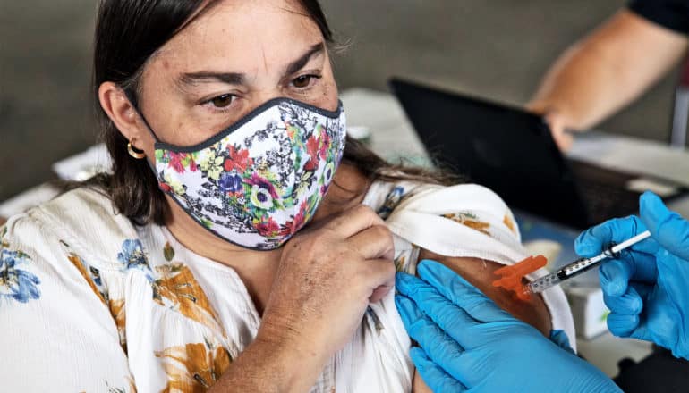 A woman gets a booster shot of the covid-19 vaccine while wearing a flower print dress and face mask