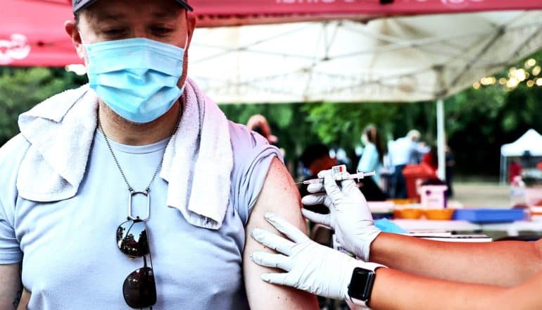 A man wearing a medical mask gets a shot of the COVID-19 vaccine under a large tent