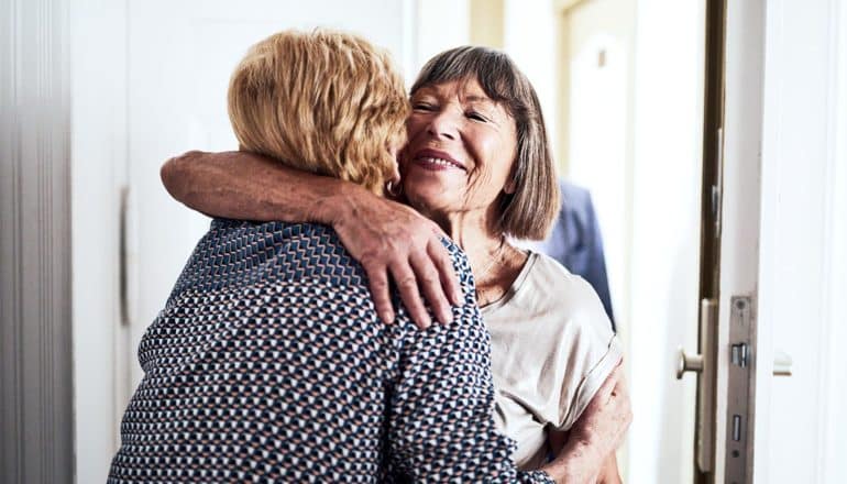 Two older women hug each other in a doorway