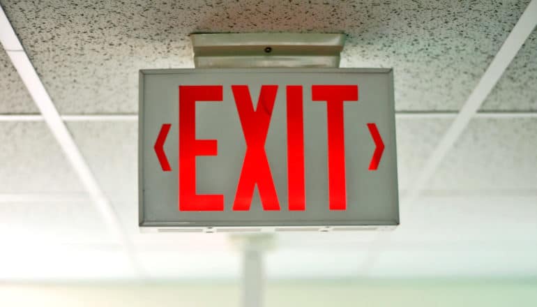 A red exit sign on the ceiling of an office