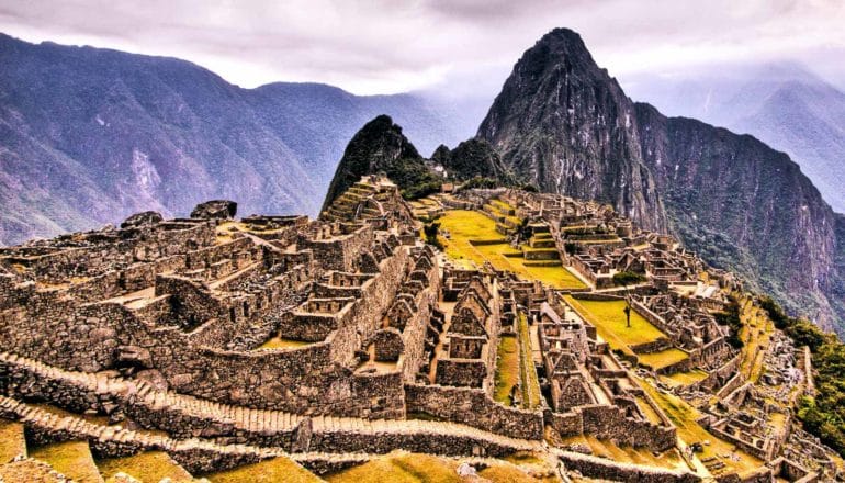 An aerial shot of Machu Picchu shows the ruins on the plateau in front of a mountain range