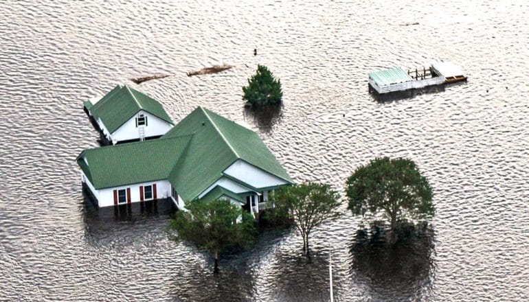 A house with a green roof sits in deep flood water after a hurricane