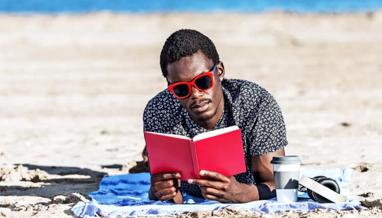 A man reads a book while laying on a towel on the beach