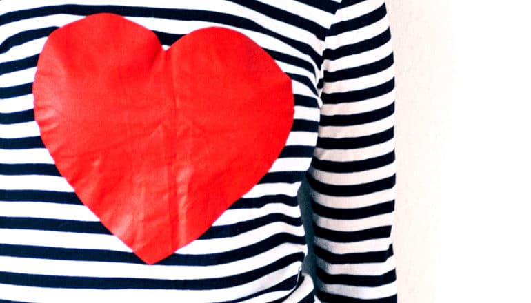 A person wears a black and white striped shirt with a large red heart on it