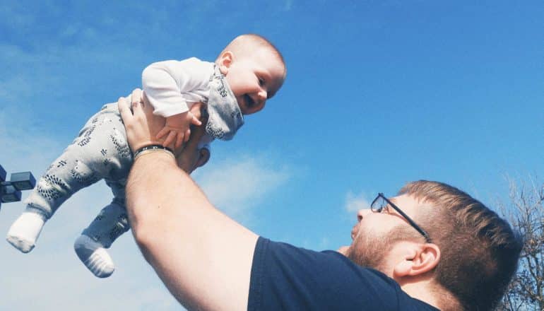 adult holds baby in air outdoors