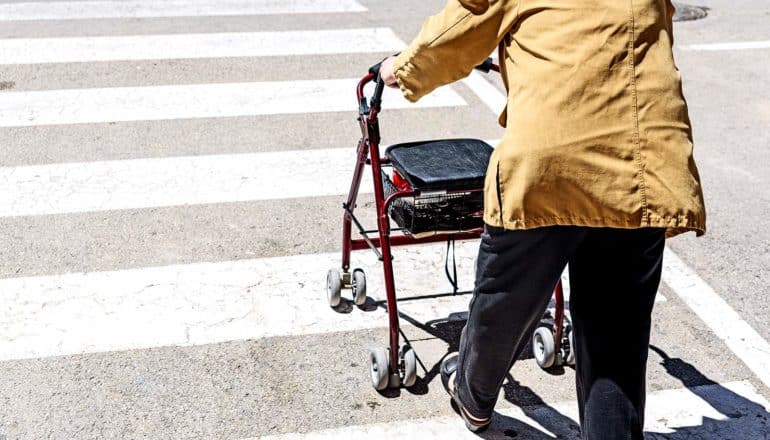 An older adult uses a walker to cross a street in the crosswalk