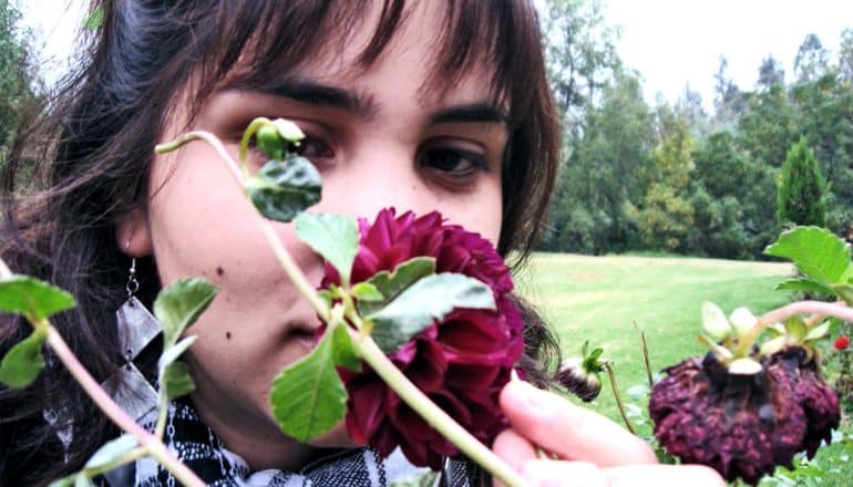 A woman smells a flower in a park