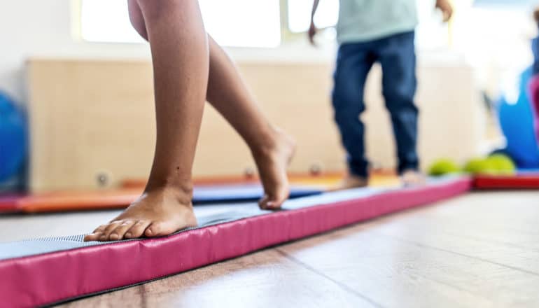 A young child walks on a foam balance beam on a wooden floor