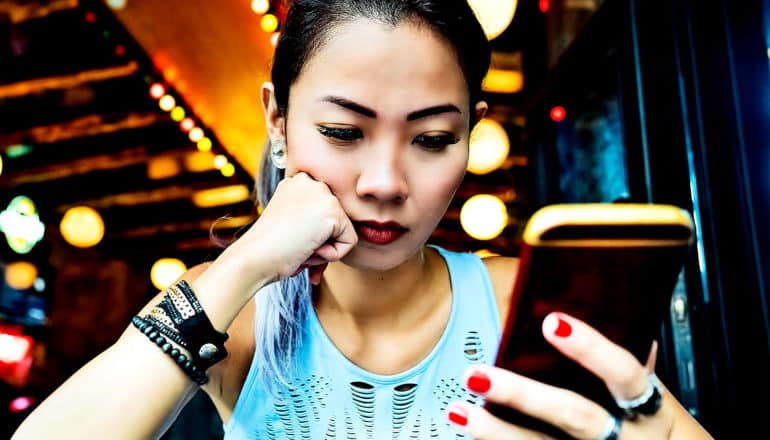 A woman rests her head on her fist as she reads her phone