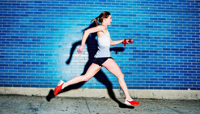 A woman runs on the sidewalk in front of a blue tile wall