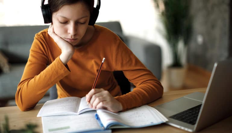 young person in headphones with laptop and notebooks