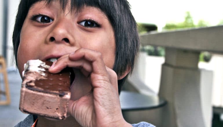 A young boy eats an ice cream sandwich with eyes wide