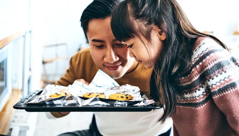 A father and daughter smell a tray of freshly baked cookies