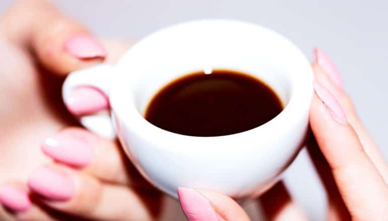 A woman with pink nails holds a small white cup of coffee