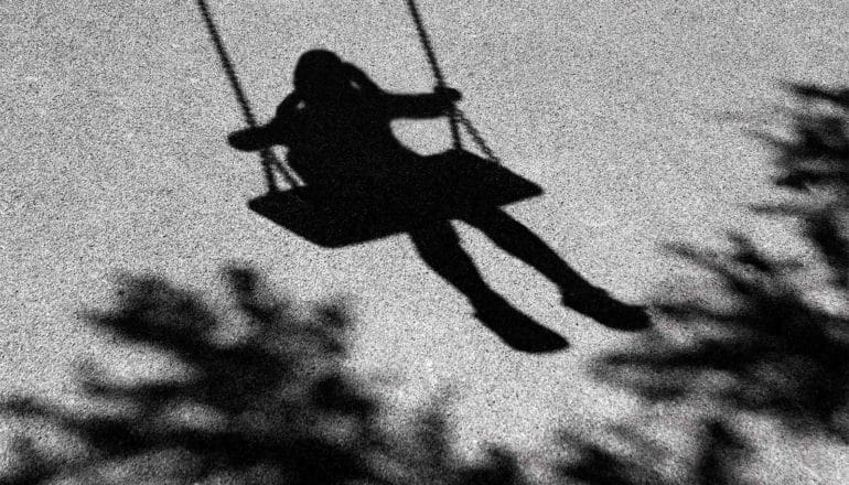 A shadow of a young child on a swing on asphalt