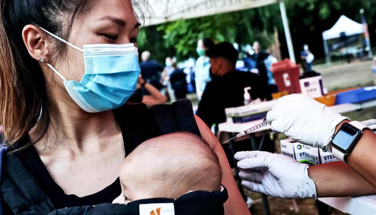 A woman holding her baby in a carrier in front of her gets a COVID-19 vaccine