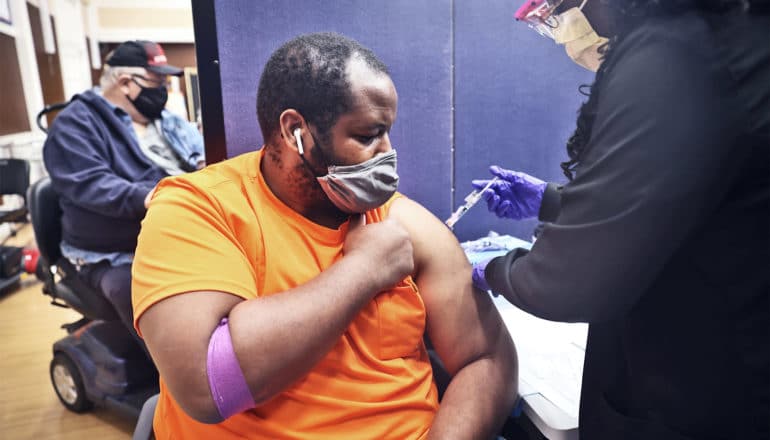 A man in an orange t-shirt gets the covid-19 vaccine