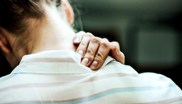 A woman holds the back of her neck with her hand