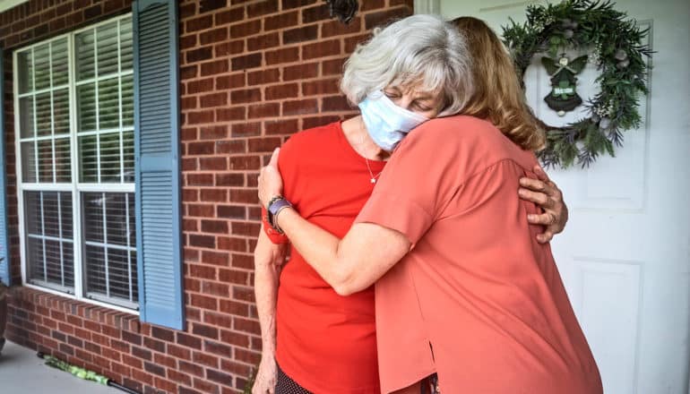 adult hugs elderly person on front porch