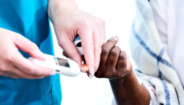 A health care worker checks an older patient's blood sugar levels