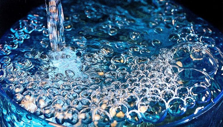 A glass of water filled to the brim has bubbles forming at the surface