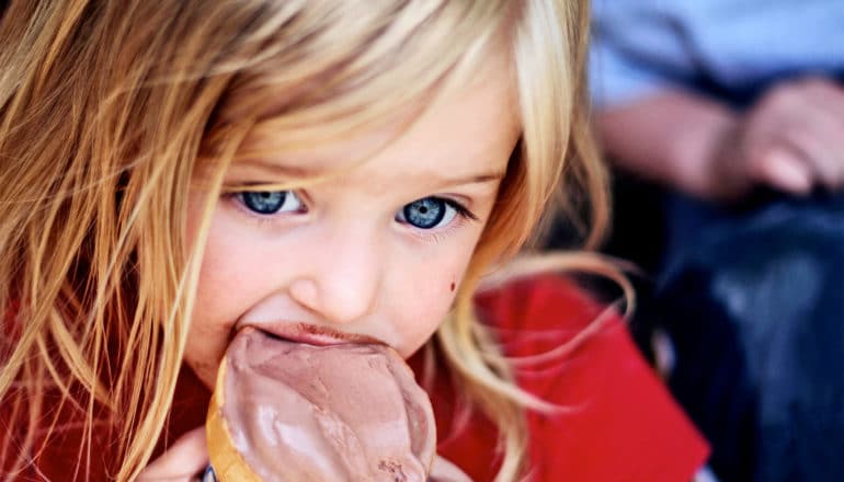 A young blonde girl eats a chocolate ice cream cone