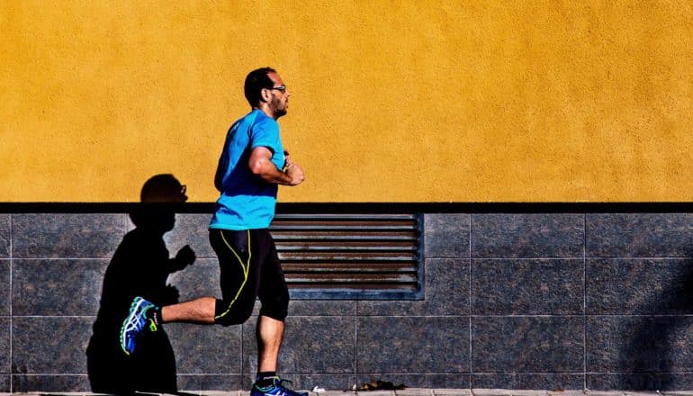 A man runs down the sidewalk against a yellow wall